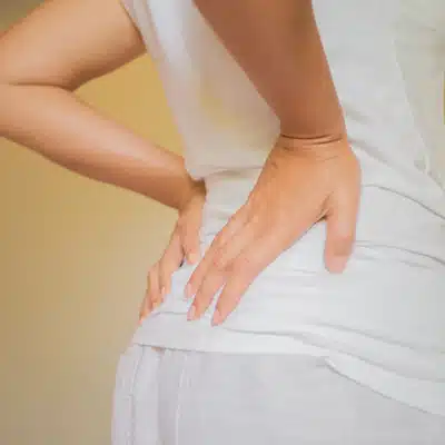 Person in white shirt holding lower back, representing low back pain chiropractor consultation or treatment