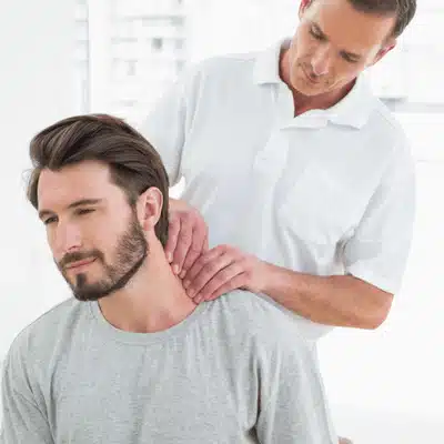 Clinician examines seated man's neck muscles and joints, palpating tender areas during rehabilitation appointment today