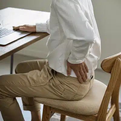 Man sits at desk holding back, planning appointment with lower back pain doctor for care