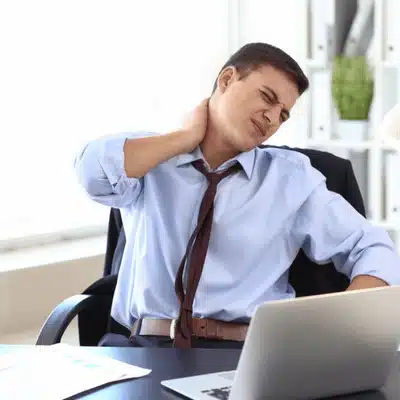 Man at office grasps neck, wincing from pinched nerve in neck during prolonged computer use