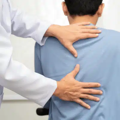 Doctor supports seated patient’s back during checkup, explaining degenerative disc disease treatment steps for recovery