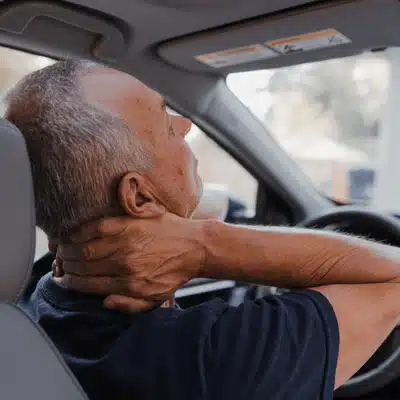 Older driver in car holds neck painfully, wondering how to treat whiplash after minor collision.