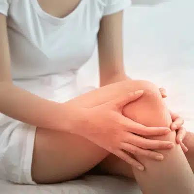 Woman holds aching knee with redness highlight, showing inflammation concerns and arthritis pain treatment options