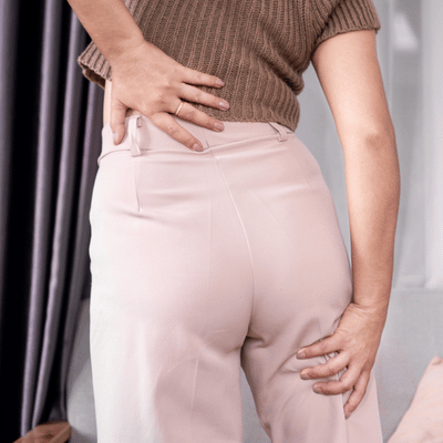 Person grasps lower back and hip, indicating sciatica or joint pain needing evaluation and treatment