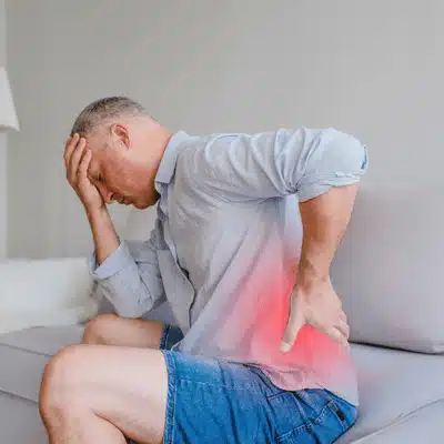Photo shows man seated holding lower back with pain highlight, seeking urgent back treatment