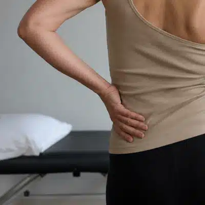 A person holds their lower back in a clinic room while showing discomfort linked to scoliosis pain relief