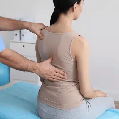 Provider presses lower back gently while patient sits for scoliosis pain relief treatment and comfort