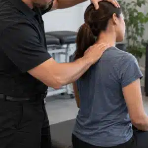 A car accident chiropractor examines a seated woman’s neck and upper back during a clinical assessment