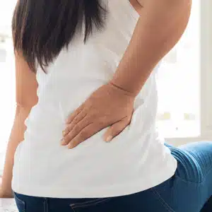 A woman touches her back, highlighting the difference between lower back pain and sciatica