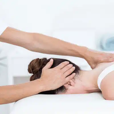 Therapist performs gentle manual therapy on woman's neck while she lies face down relaxing comfortably