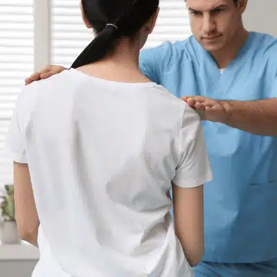 Clinician assesses shoulder level with hands raised for scoliosis pain relief evaluation in clinic