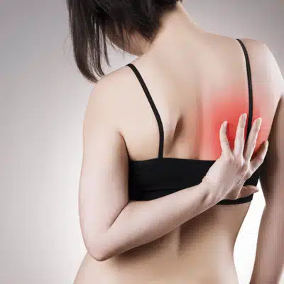 Woman scratches upper back with red pain area, indicating trapped nerve in shoulder blade discomfort