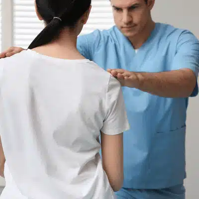 Provider assesses shoulder height and posture during scoliosis treatment near me consultation in office