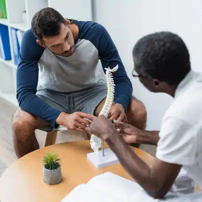 Patient and chiropractor examine spine model during discussion, focusing on whether can a chiropractor help with sciatica