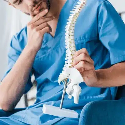 Clinician studies vertebral model, explaining degenerative disc disease vs herniated disc differences to patient today