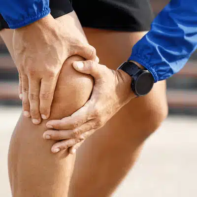 Athlete clutches sore knee outdoors, close-up of injury signs requiring arthritis pain treatment evaluation prompt