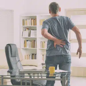 A man stands up holding his back, showing difference between lower back pain and sciatica