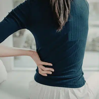 Woman holds lower back near waistline, seeking lower back pain doctor for diagnosis and relief