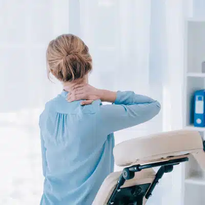 A woman in an office rubs her neck, questioning can a chiropractor fix a pinched nerve