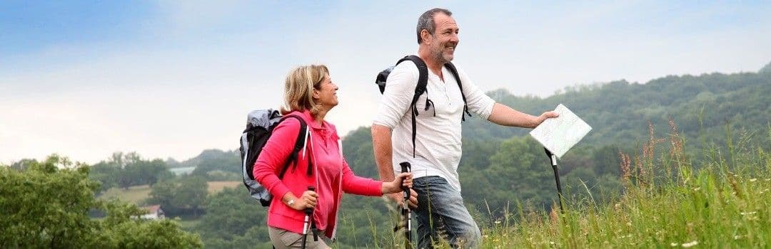 active-couple-hiking-green-hills Active couple hiking with backpacks and trekking poles through green hills