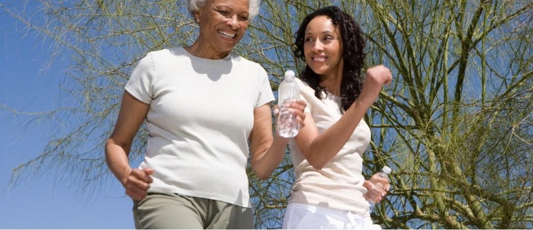 women-jogging-with-water-bottles Two smiling women jogging outdoors with water bottles under a blue sky